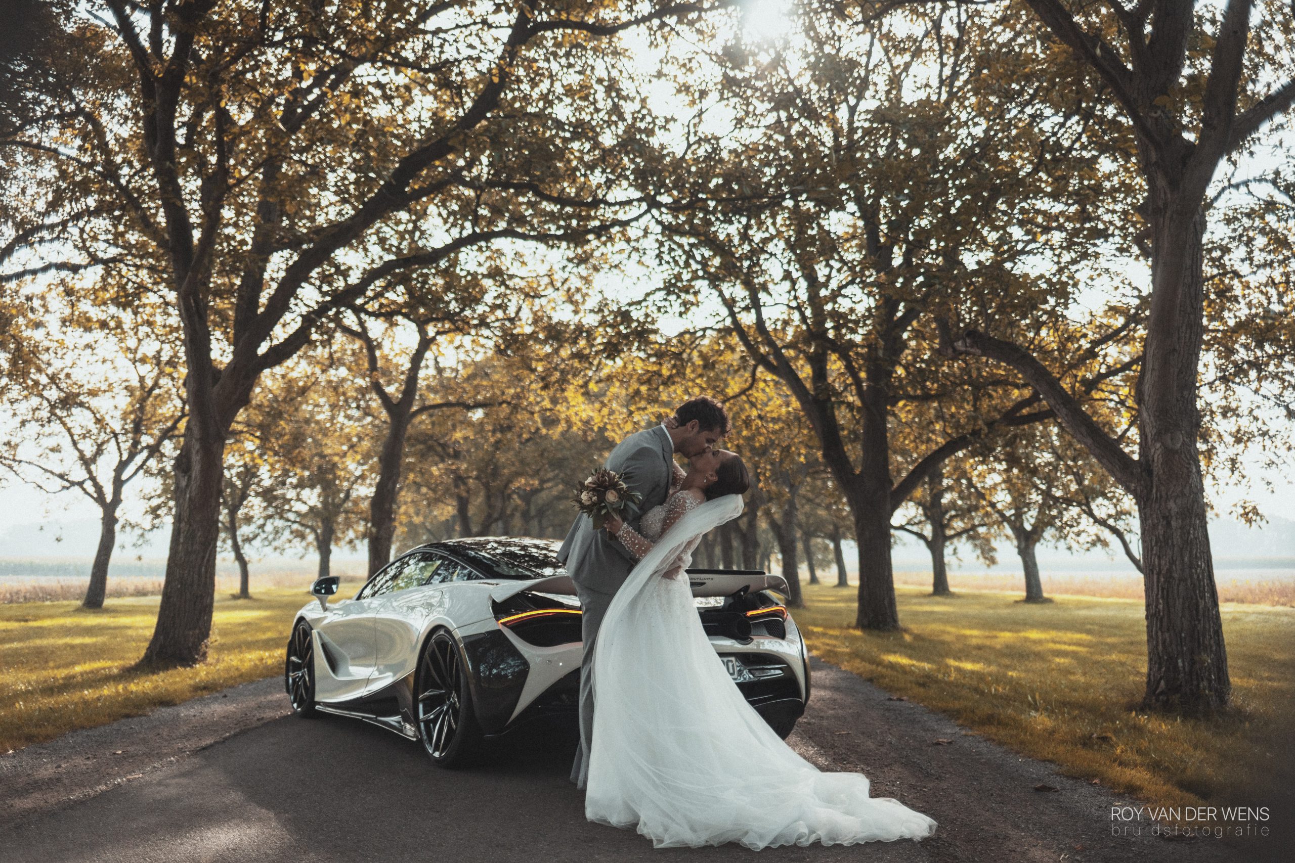 A man kissing his bride in front of a supercar.